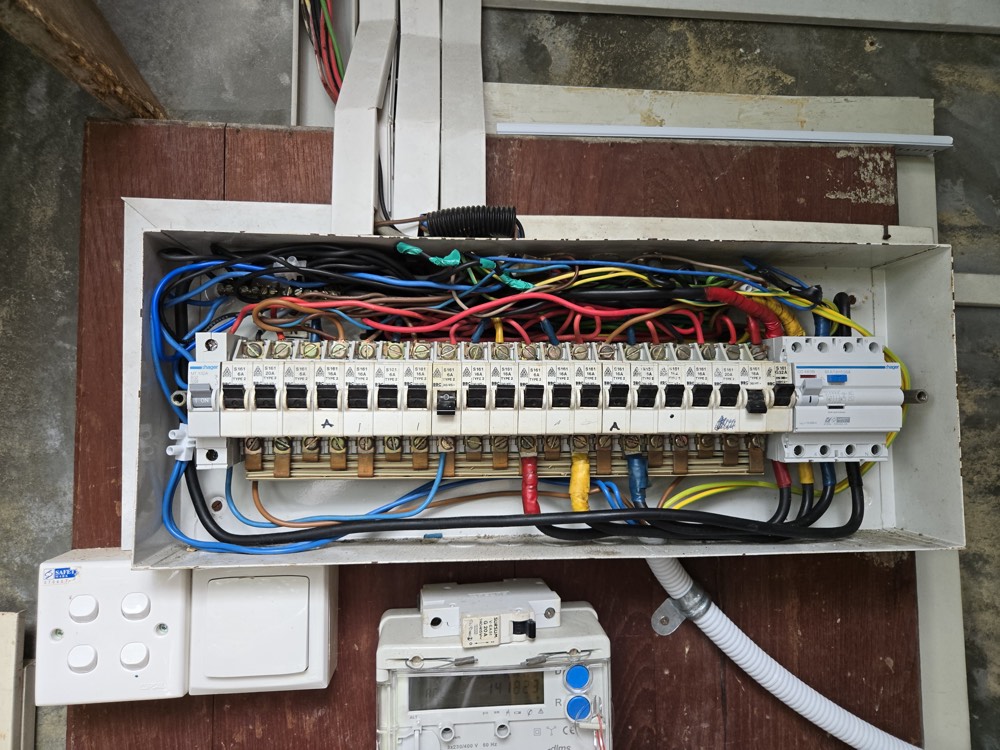 An opened consumer unit with tangled wiring being tidied and made safe
