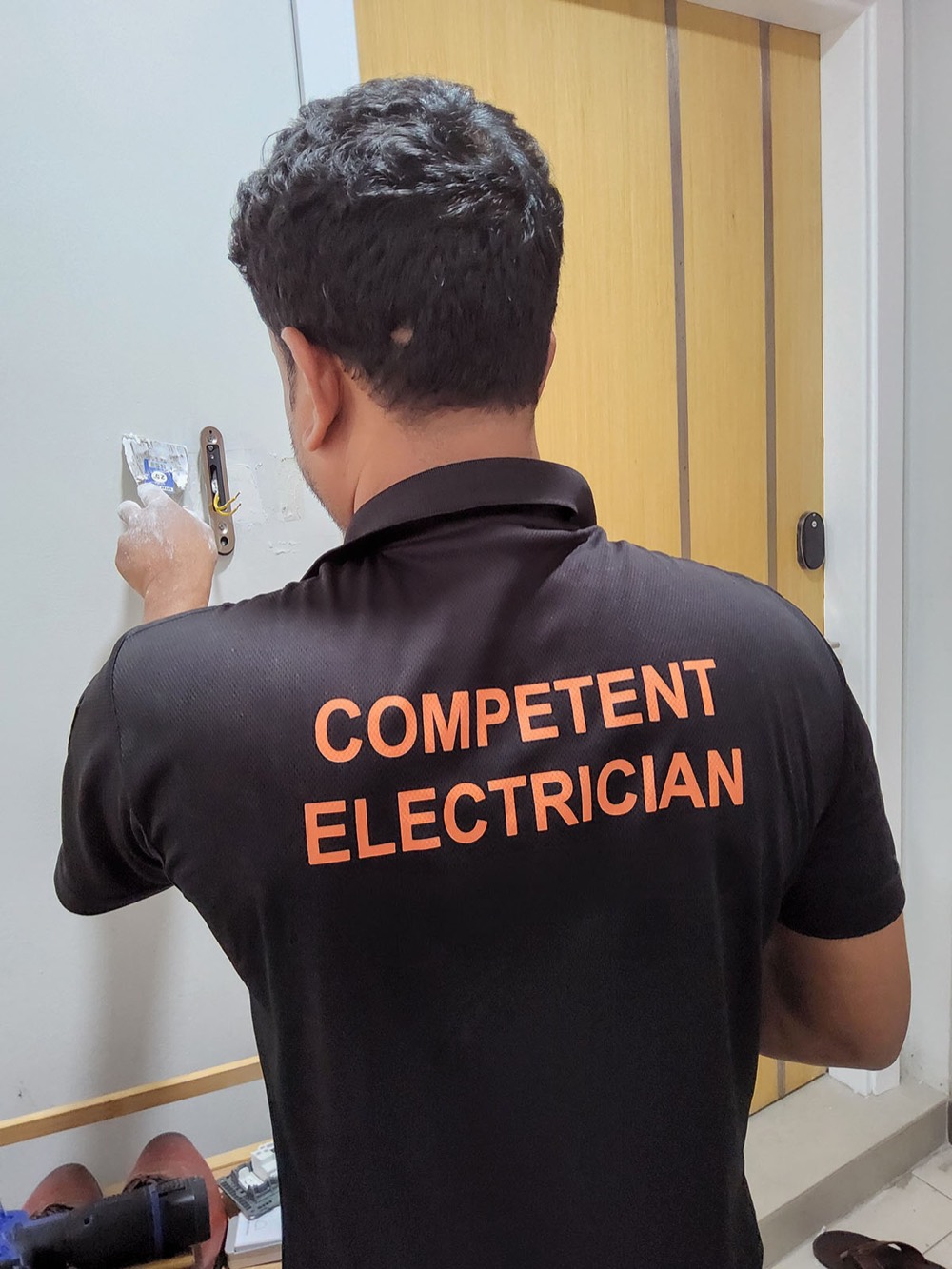 Competent Electrician crew member in a branded COMPETENT ELECTRICIAN uniform polo on a job