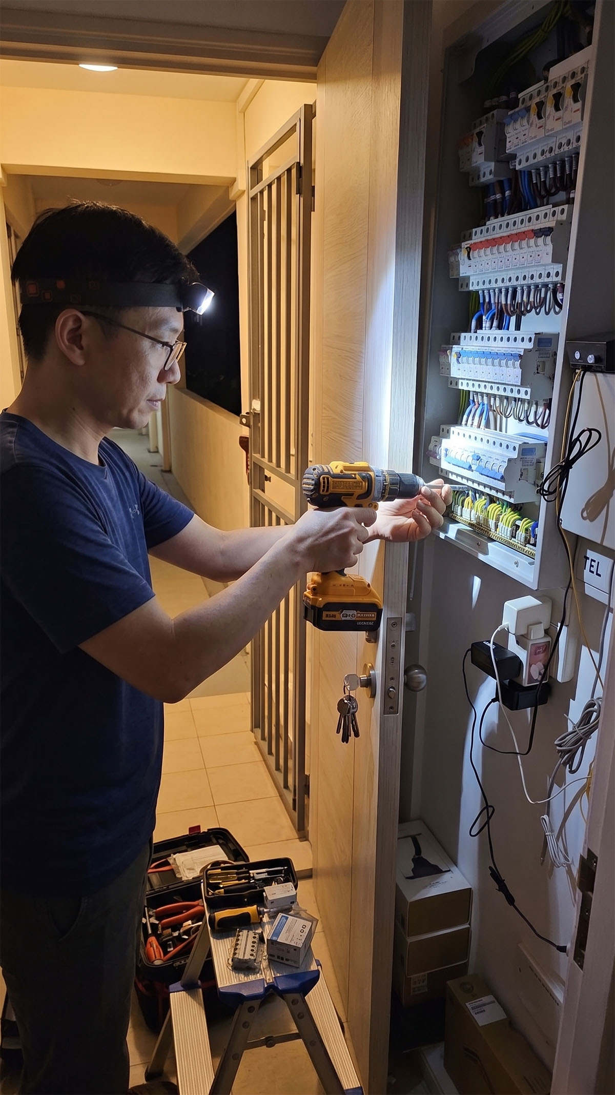 EMA-licensed Competent Electrician working on an HDB distribution board at night, headlamp on, toolbox open