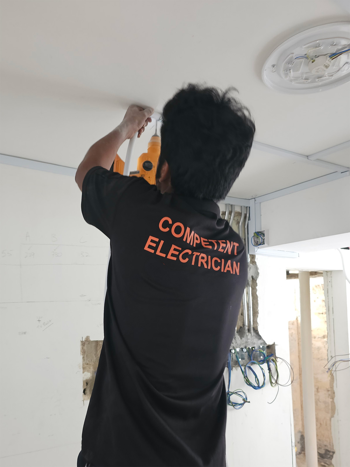 Competent Electrician in branded uniform drilling a ceiling fixture